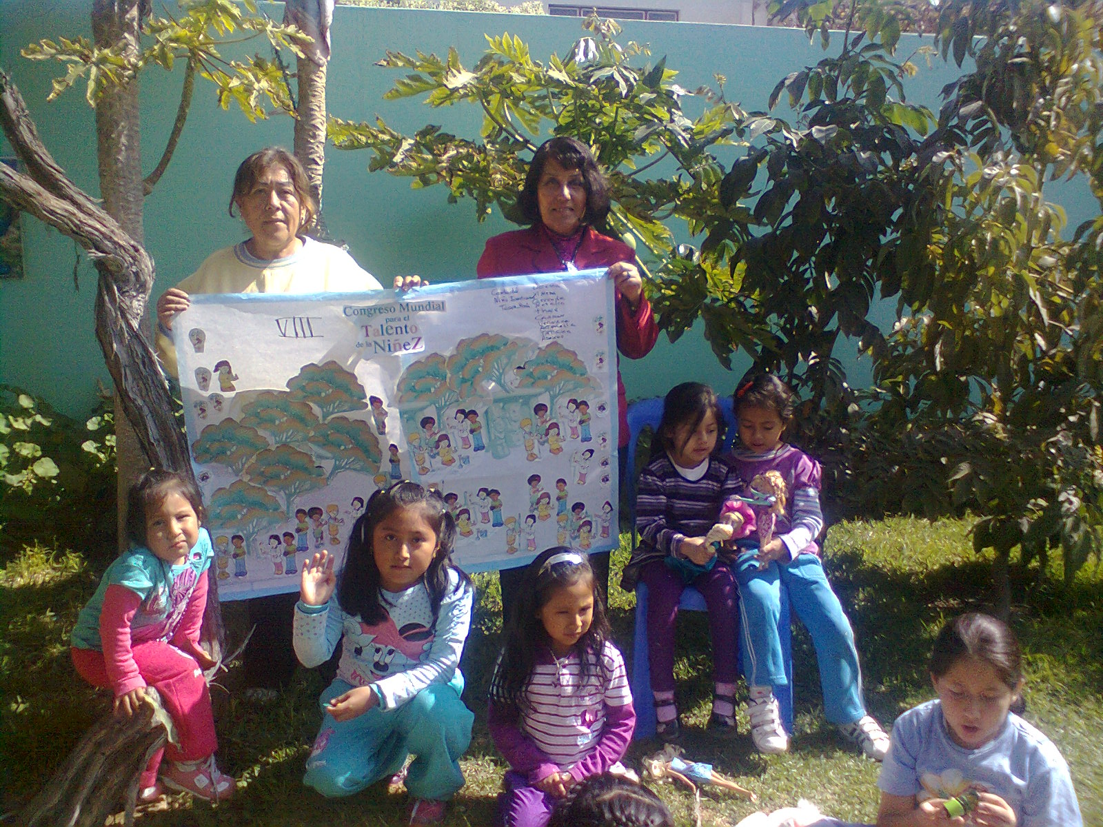 DOCENTRES Y NIÑAS EN EL JARDIN MOSTRANDO SU COLAGE DEL ARBOL